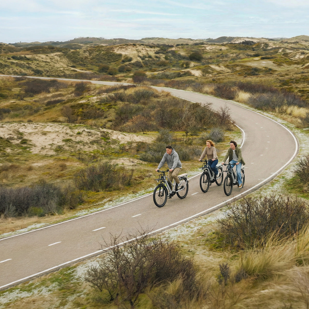 Drei Personen fahren auf Simply.Lift EP6 Longtail E-Lastenrädern hintereinander auf einem kurvigen Radweg durch eine hügelige Dünenlandschaft.