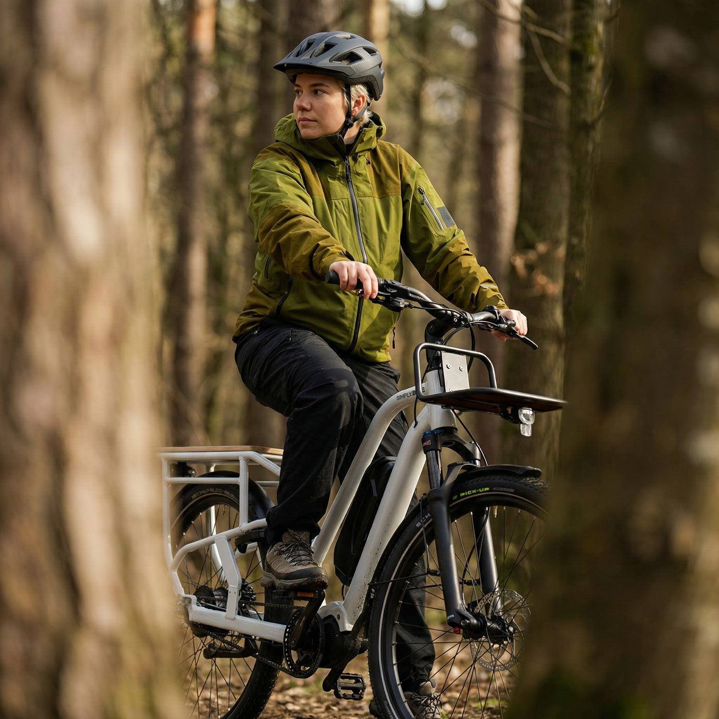 Person fährt ein Simply.Lift EP6 Longtail E-Lastenrad mit Frontgepäckträger und Federgabel auf einem unbefestigten Waldweg.