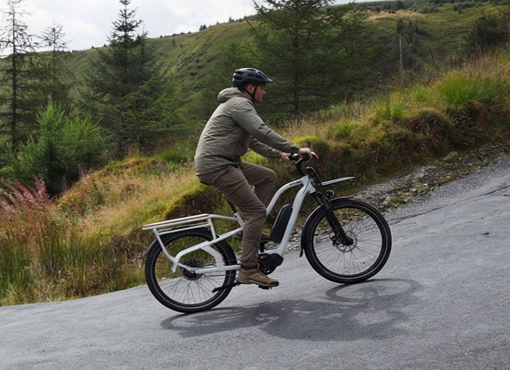 Simply.Lift EP6 Longtail E-Lastenrad mit Frontgepäckträger eine steile, kurvige Straße in einer hügeligen Naturlandschaft.