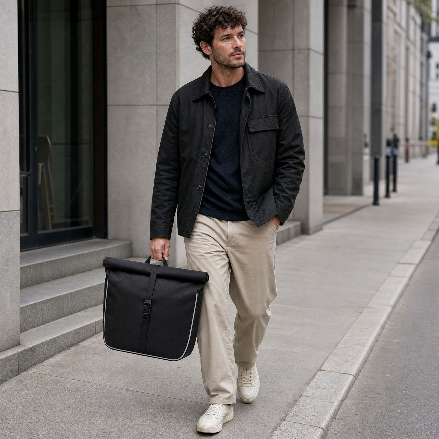 Mann trägt schwarze Packtasche des Simply.Lift EP6 E-Lastenrads am Tragegriff durch die Stadt.