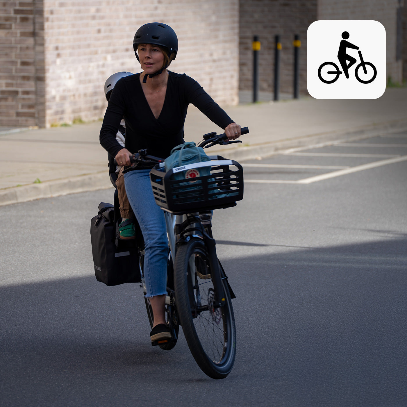 Frau fährt mit Kind auf dem Simply.Lift EP6 E-Lastenrad, beladen mit Packtasche und Frontkorb, durch die Stadt.