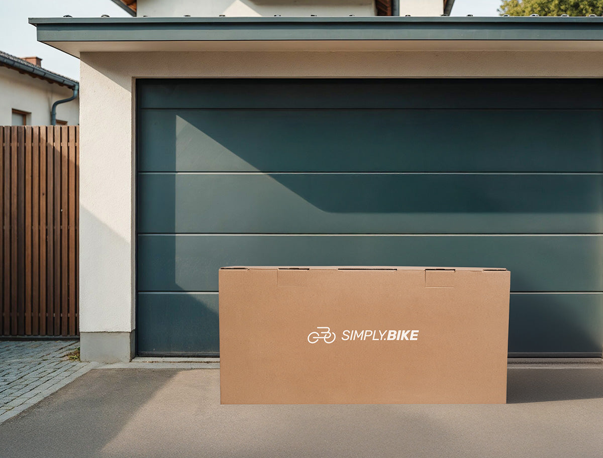 Versandkarton mit dem Simply.Bike Logo steht auf einer Einfahrt vor einer Garage und zeigt die sichere Lieferung eines E-Lastenrads direkt nach Hause.