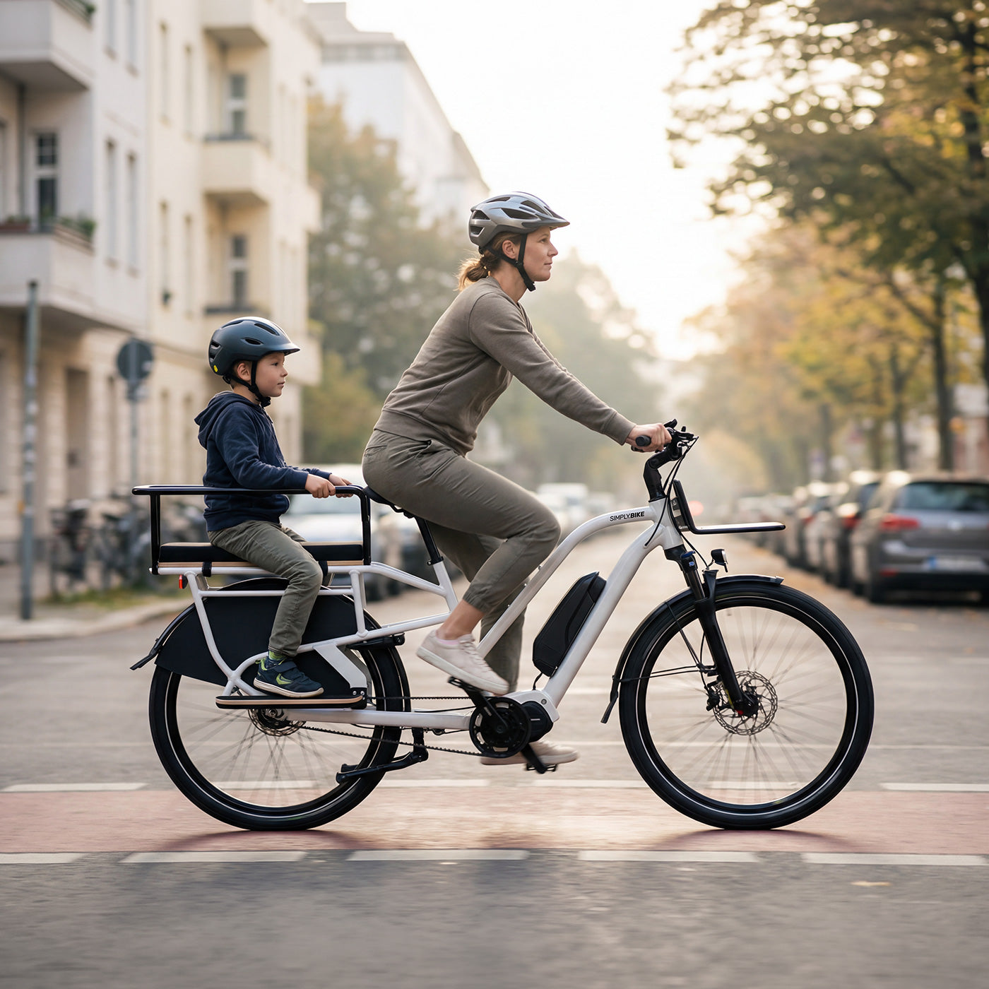 Eine Frau fährt ein Simply.Lift EP6 Longtail E-Lastenrad mit einem Kind im Sicherheits-Handlauf auf einer städtischen Straße.