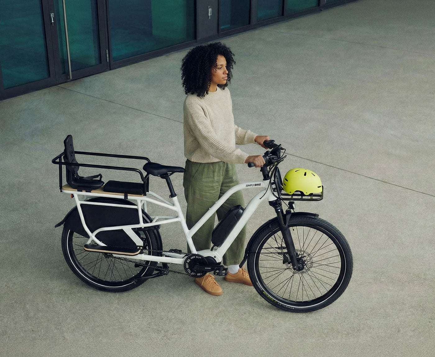 Eine Person steht neben einem Simply.Lift EP6 Longtail E-Lastenrad mit montiertem Sicherheits-Handlauf, hinterem Kindersitz und Frontgepäckträger.