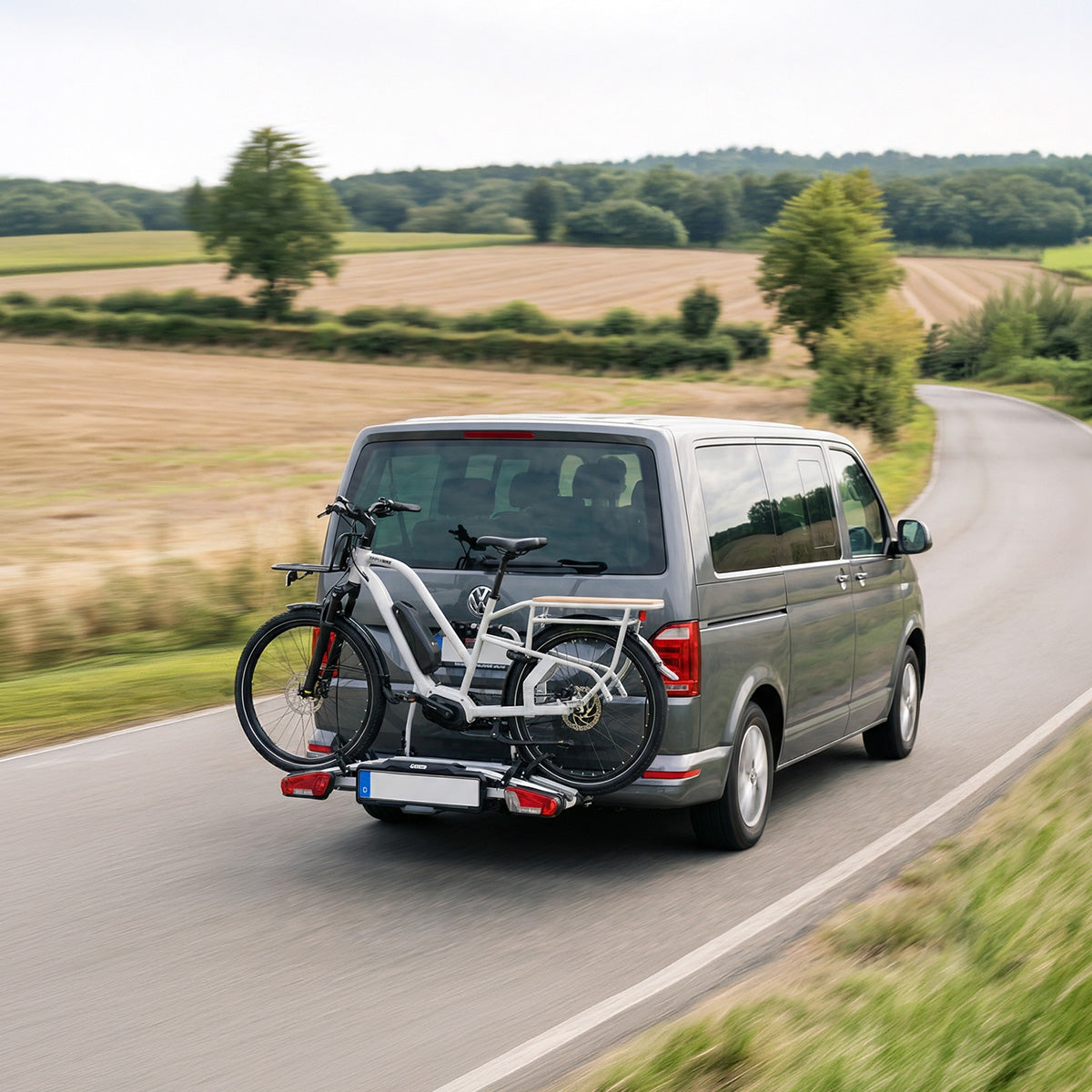 Weißes Simply.Lift EP6 E-Lastenrad auf dem Heckträger eines Vans auf einer Landstraße.