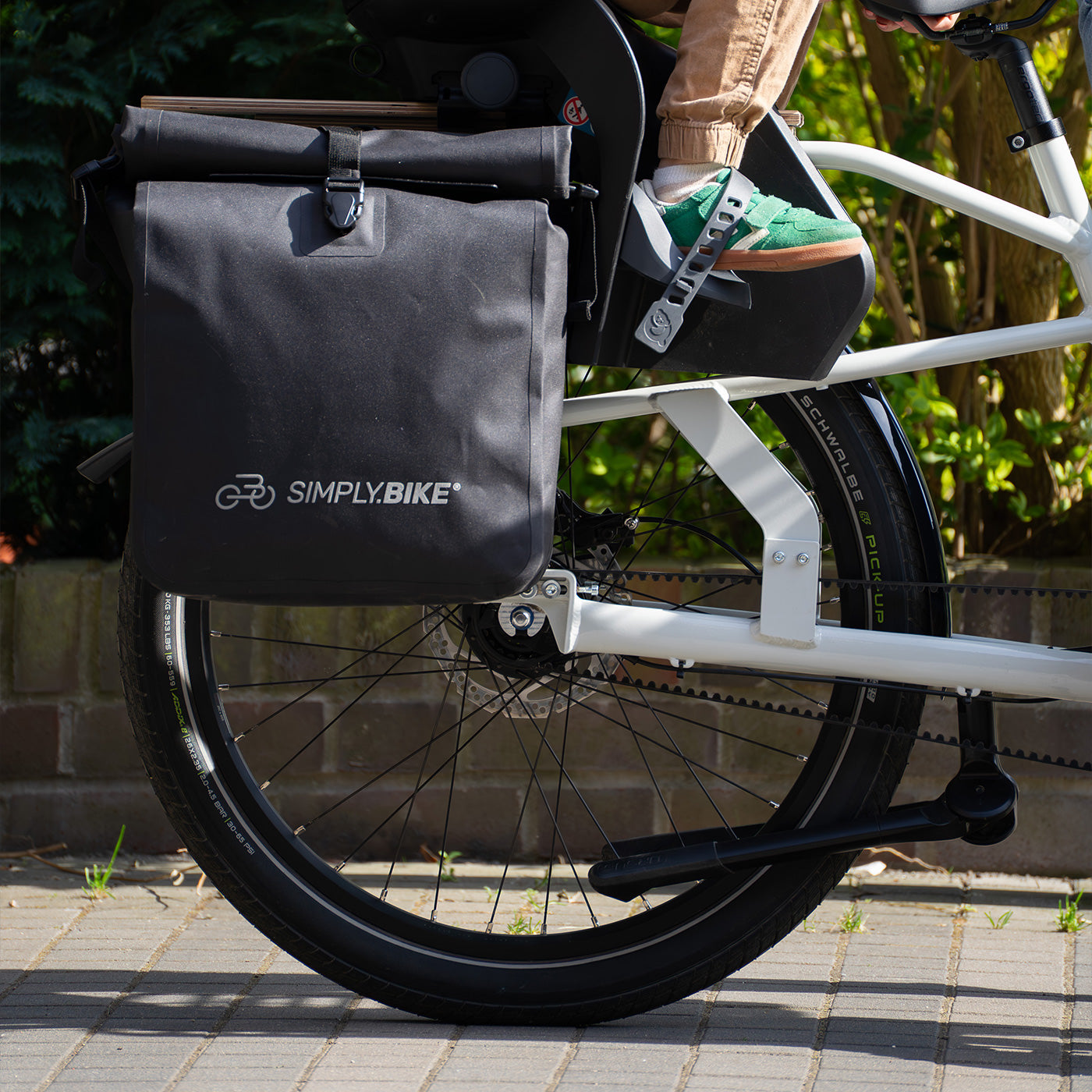 Schwarze Simply.Bike Packtasche am Heck des weißen Simply.Lift EP6 E-Lastenrads, mit Kind auf dem Trittbrett.
