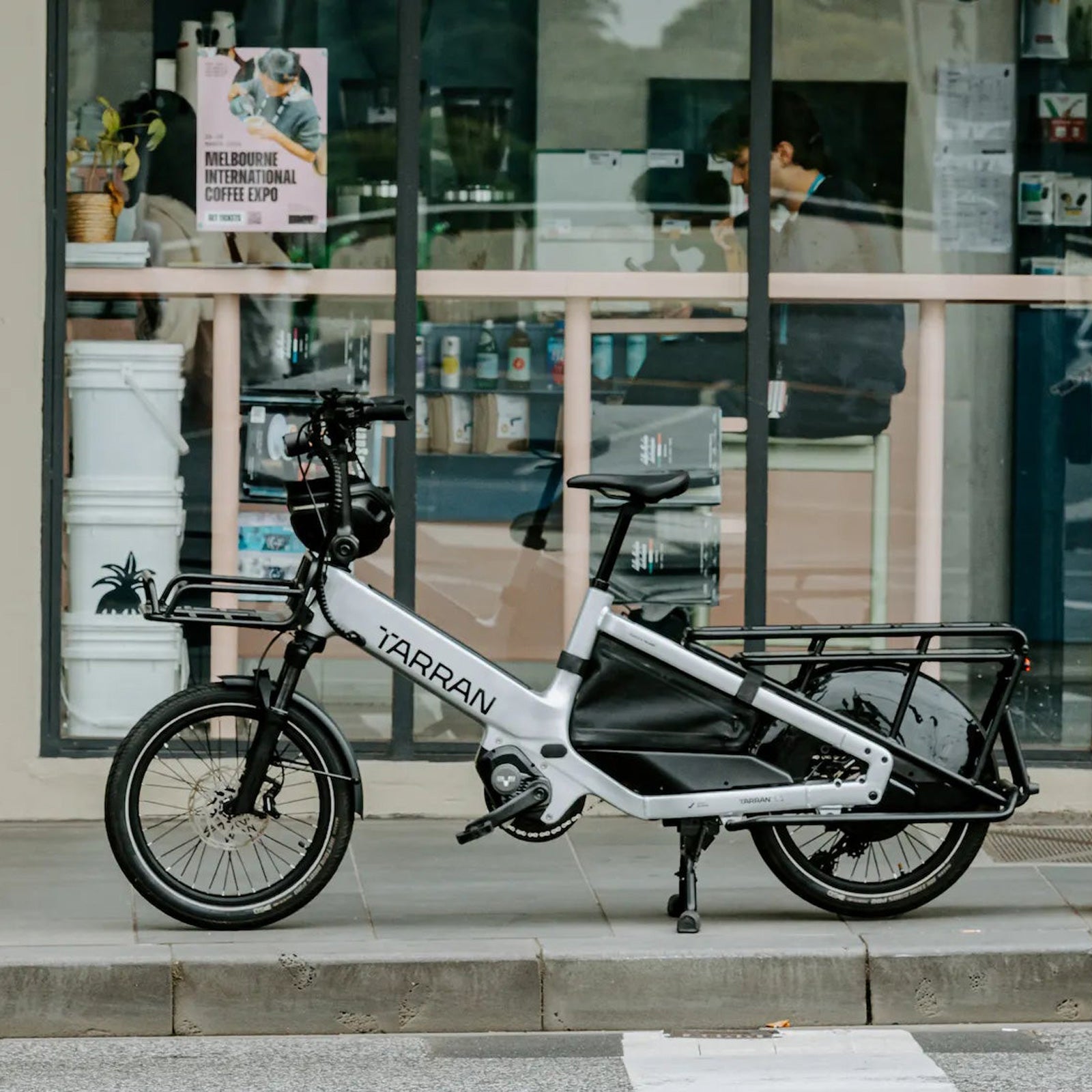 Tarran L1m in Hellgrau am Straßenrand vor einem Café, Seitenansicht mit Frontträger, Heckträger und Rahmentasche